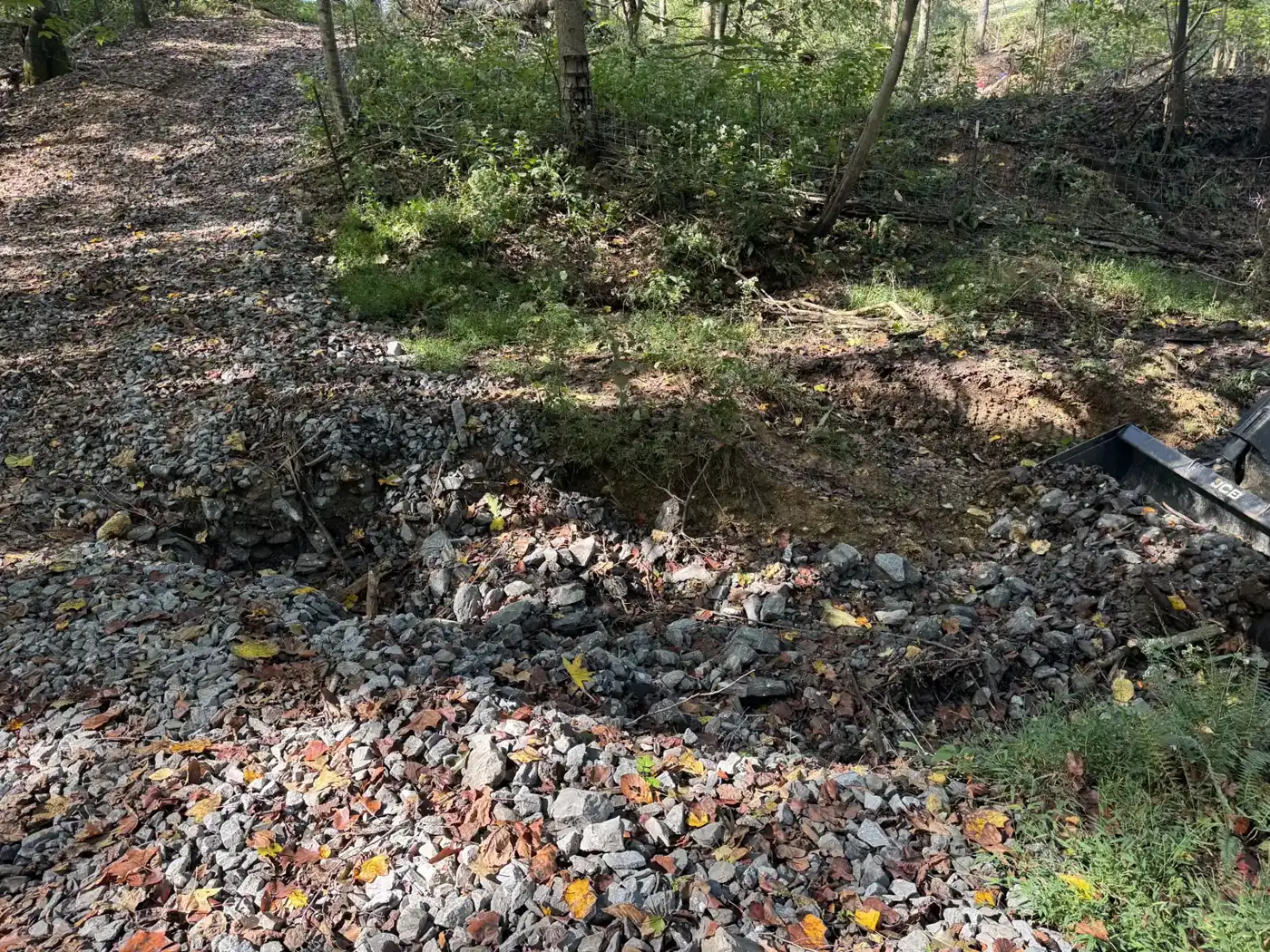 Close-up of the rain-washed hole in a gravel woods road in Westmoreland, TN, with a machine bucket edge at right