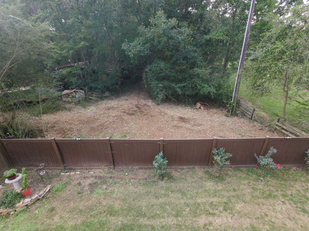 After forestry mulching: brush cleared behind the same backyard fence, leaving open ground covered in mulch
